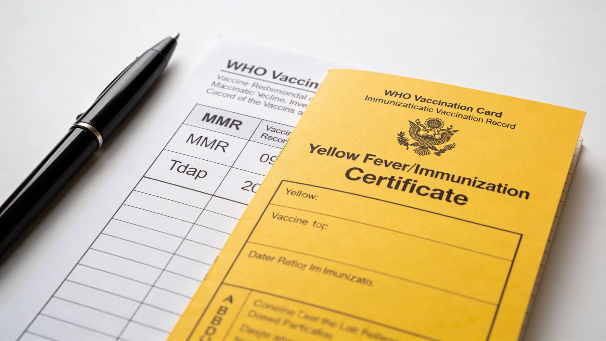 A black pen lies next to a WHO vaccination record card and a yellow fever immunization certificate.